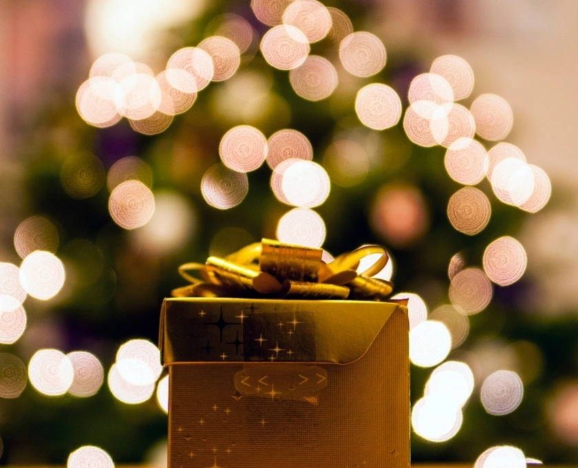 A Christmas present in a gold gift box with Christmas lights in the background