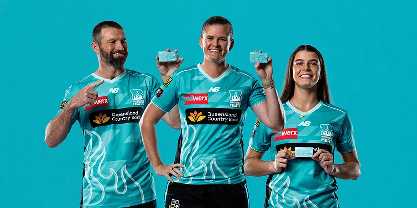 Three Brisbane Heat players hold Queensland Country Bank Brisbane Heat branded debit cards against a teal background.