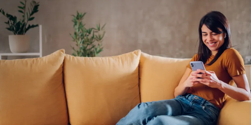 A person sitting on a sofa using a smartphone, with indoor plants in the background.