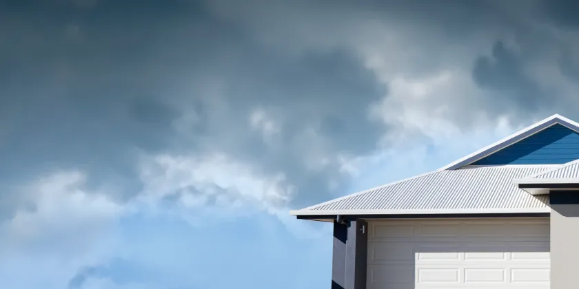 Suburban home with a light metal roof under threatening storm clouds, representing storm preparedness and home protection.