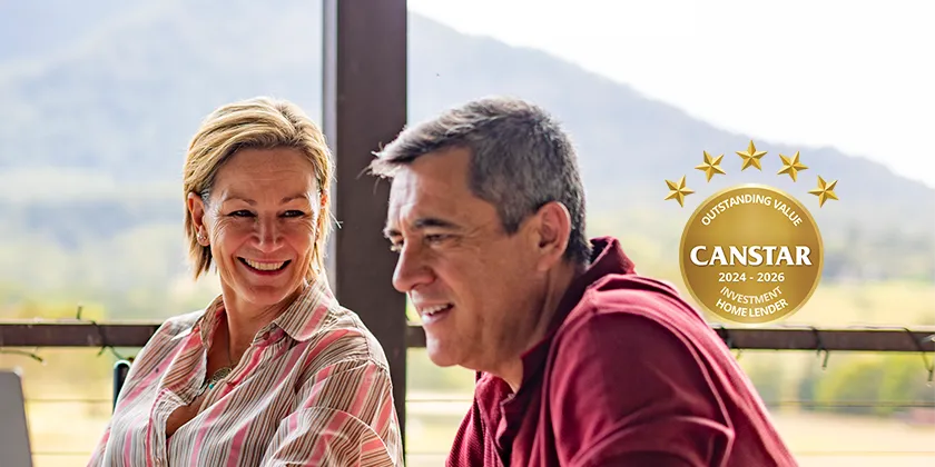 Two people sitting outdoors with a laptop on a veranda overlooking a mountain landscape, with a Canstar Outstanding Value Investment Home Lender 2024-2026 award badge displayed.