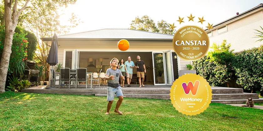 A child playing with a ball in a backyard in front of a family home, with three adults standing on a deck and Canstar Bank of the Year Customer-Owned 2023-2025 and WeMoney Best for Value Fixed Home Loans Banking 2025 award badges displayed.