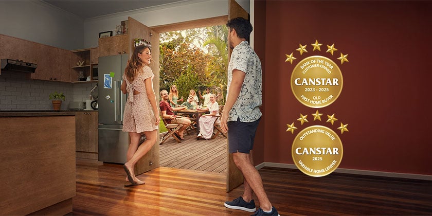 Two people inside a modern kitchen looking out to a wooden deck where a group of people are seated around a table. Two gold Canstar award badges are shown on the right side of the image.