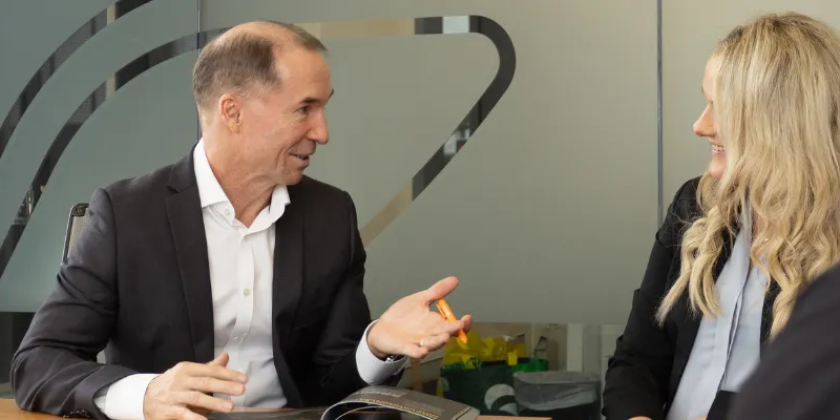Two professionals seated at a table in a modern office engaged in conversation.