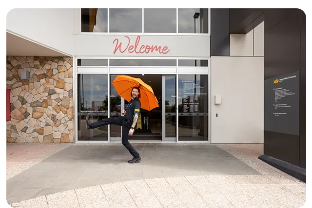 Person posing playfully outside Queensland Country Centre building entrance with a welcome sign.
