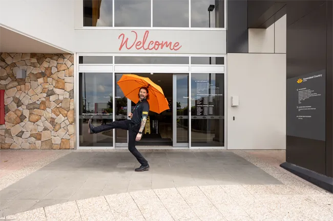 Person posing playfully outside Queensland Country Centre building entrance with a welcome sign