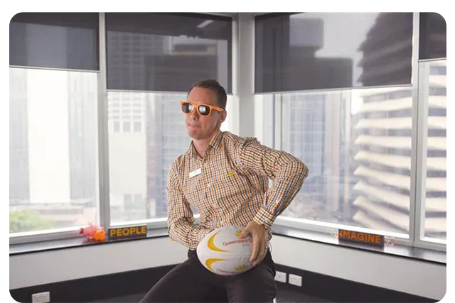 Person in a checkered shirt holding rugby ball indoors.