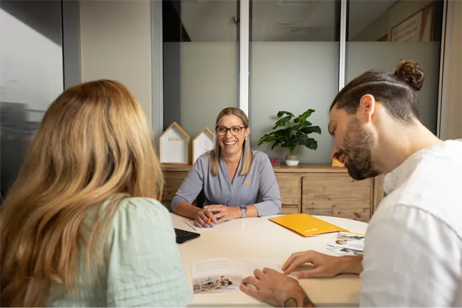 Two Queensland Country Bank members seated at a desk with a Queensland Country Bank staff member in a private office, reviewing documents during a personalised banking consultation.