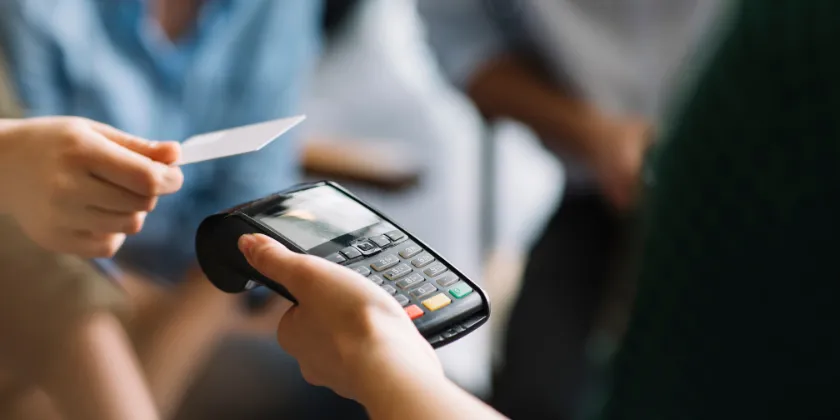 Close-up of a person holding a card above a payment terminal during a contactless transaction.