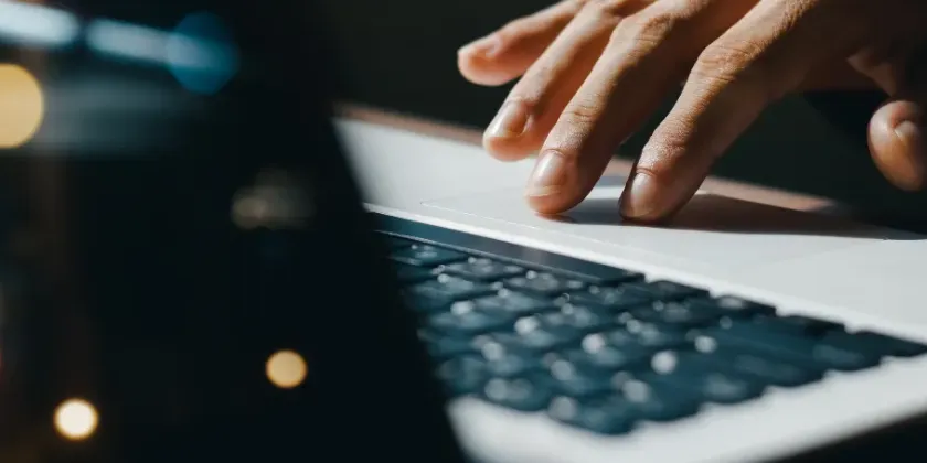 Close‑up of a hand typing on a laptop keyboard with blurred lights reflected across the screen.