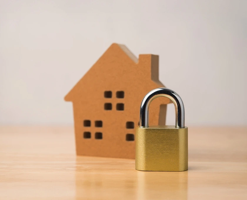A gold padlock placed in front of a small cardboard house model on a wooden surface, representing the rate lock fee offered by Queensland Country Bank.