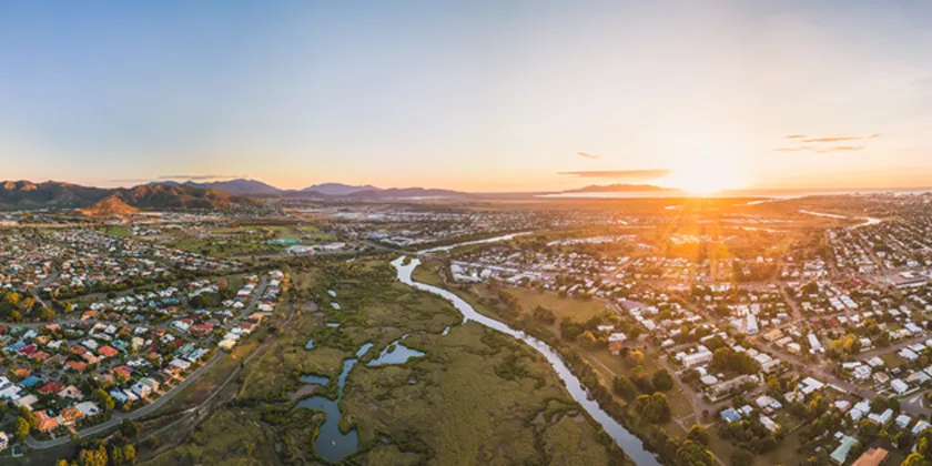 Aerial view of Townsville at sunrise, showing suburban neighbourhoods, waterways and surrounding hills.