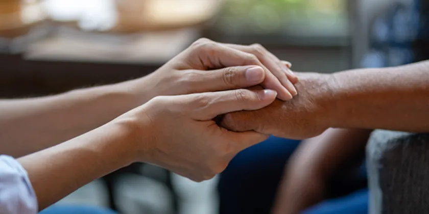 Two people holding hands in a supportive gesture, representing care, assistance and support.