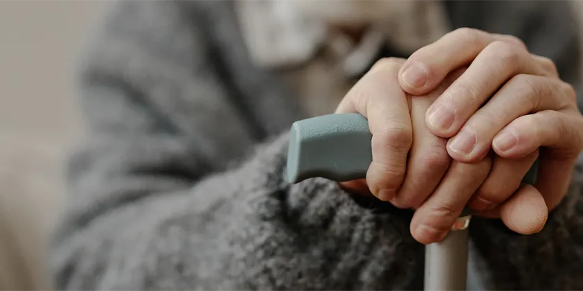 Close-up of hands resting on the handle of a walking aid, symbolising support and care for older people.