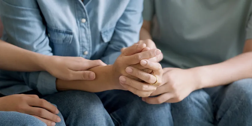 Close-up of people holding hands in a supportive gesture during a conversation.