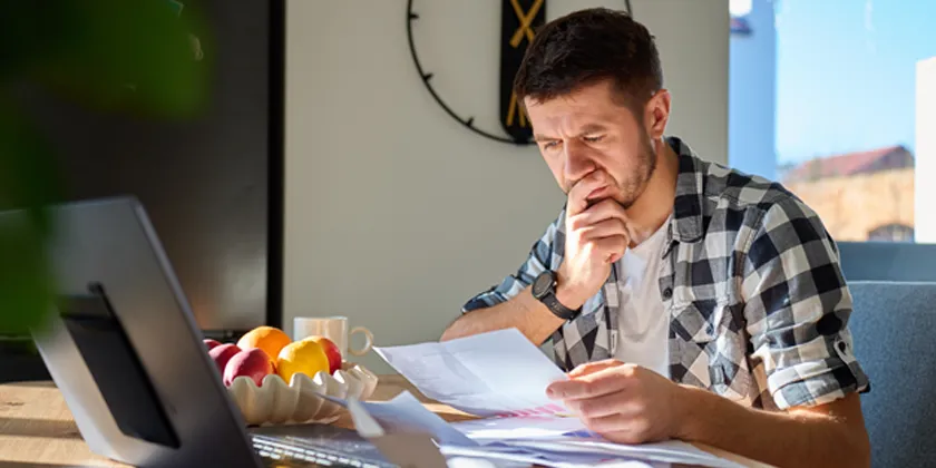 Person seated at a table reviewing bills and financial documents beside a laptop.