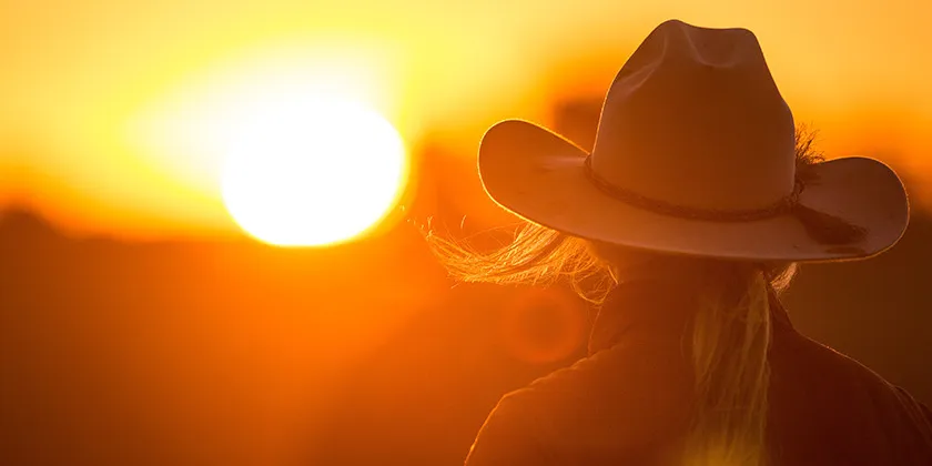 Person wearing a wide-brimmed hat watching a sunset over a rural landscape.