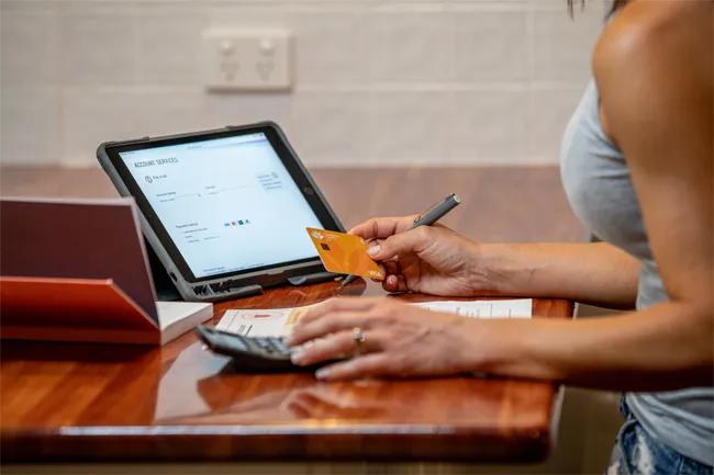Person holding a yellow Visa card while reviewing payment information on a tablet device