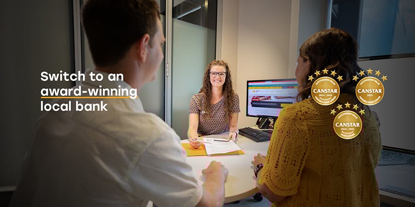 Three people seated around a table in an office setting, with one person facing the camera and speaking. Text on the left reads 'Switch to an award-winning local bank.' A gold badge on the right displays 'Outstanding Value CANSTAR 2025 Variable Home Lender' with five stars.