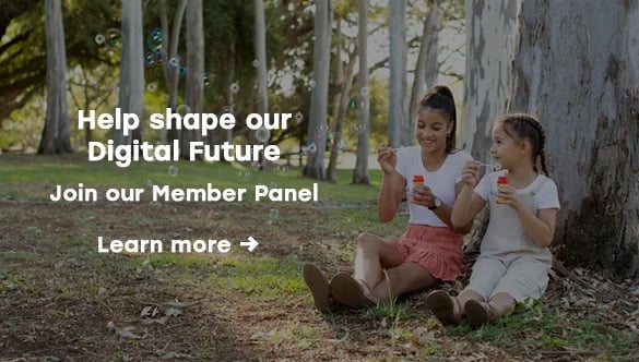 Two children sitting under trees in a park blowing bubbles, with overlaid text inviting users to join Queensland Country Bank&rsquo;s Member Panel and to &ldquo;Learn more&rdquo;.