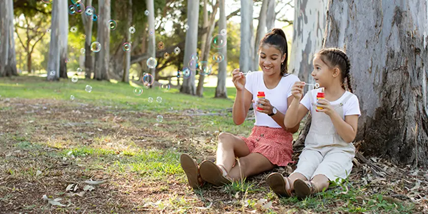 Two girls sitting in a park and blowing bubbles. 