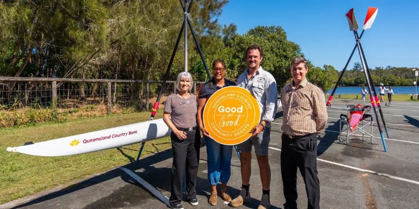 Community grant recipients standing beside a canoe holding a Queensland Country Good for Good Community Grants sign.