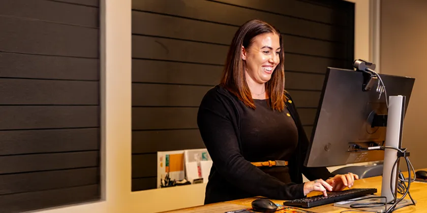 One of Queensland Country Bank’s Money Mentors standing at a computer workstation inside a modern bank branch.