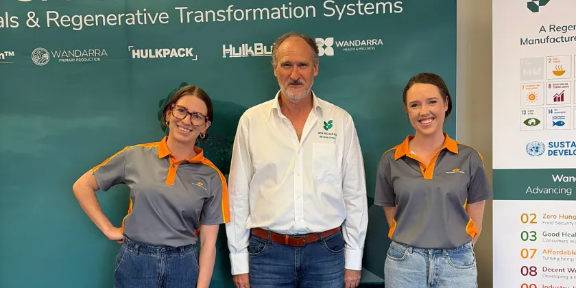 Three people pose in front of a green banner, with the centre person in a white shirt and two others in Queensland Country Bank polo shirts.