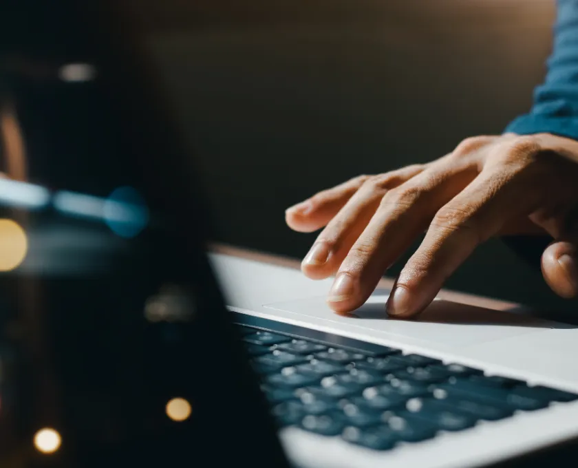 Close‑up of a hand typing on a laptop keyboard with blurred lights reflected across the screen.