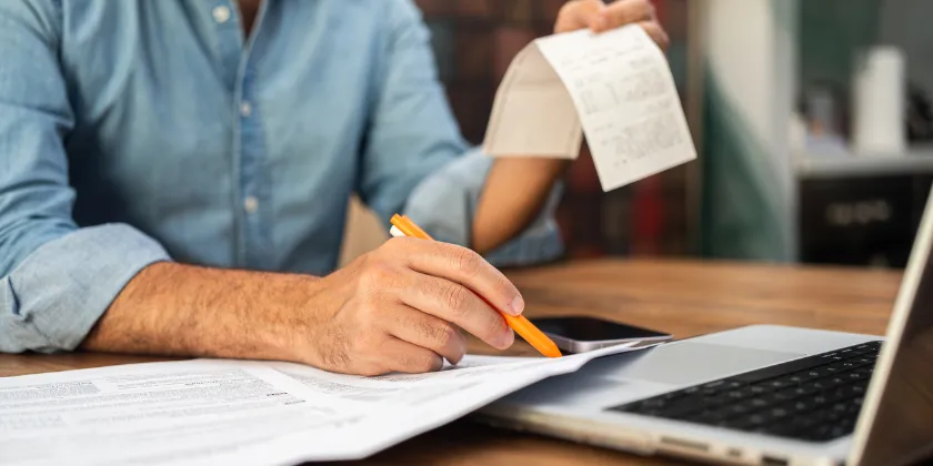 Person reviewing tax documents and a receipt while using a tablet and laptop, illustrating vigilance against ATO tax scams and protecting personal financial information.