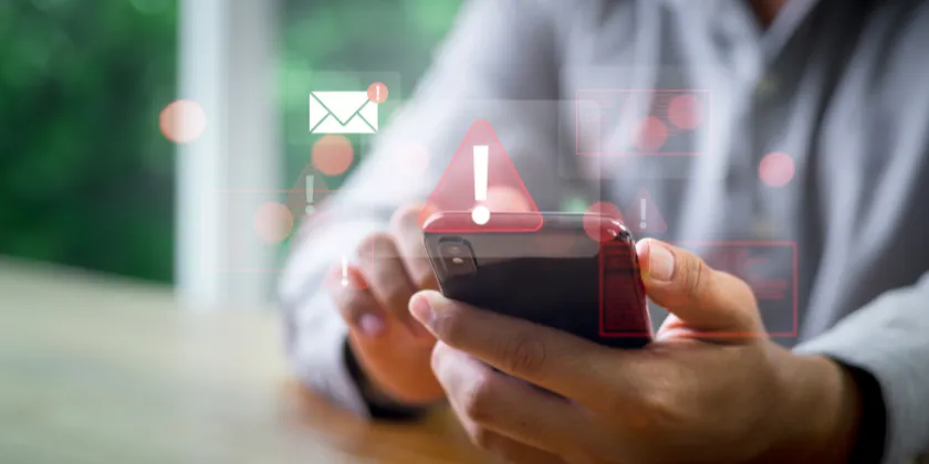 Person holding and using a smartphone, with overlaid warning and notification icons symbolising Sender ID verification on a mobile device.