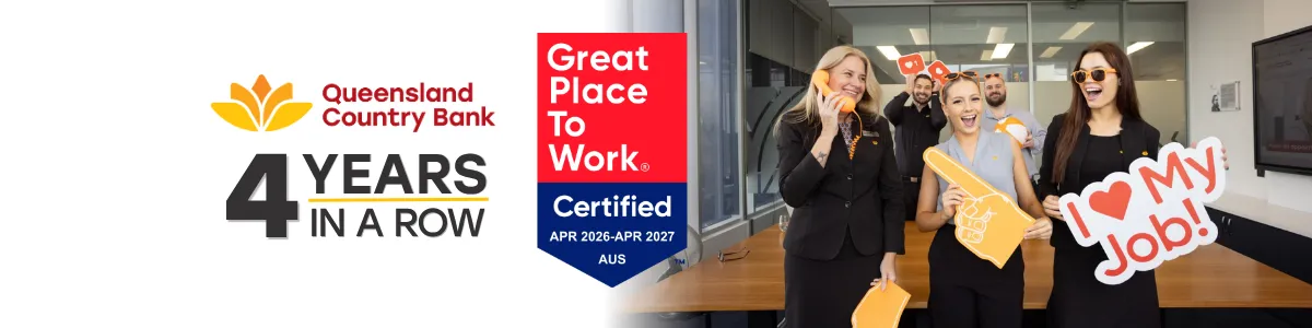 A group of Queensland Country Bank employees standing in an office holding branded props, with imagery showing “Great Place to Work Certified” and “Queensland Country Bank – 4 years in a row.”