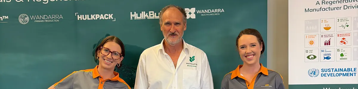 Three people pose in front of a green banner, with the centre person in a white shirt and two others in Queensland Country Bank polo shirts.