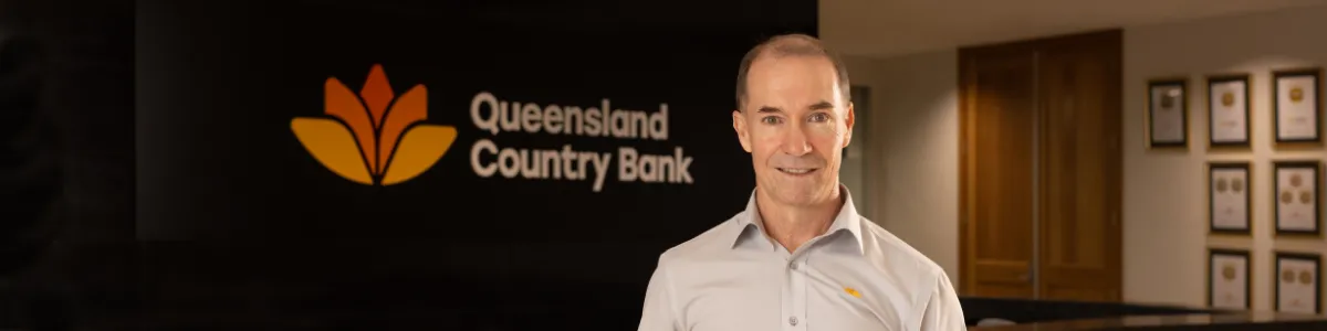 Queensland Country Bank CEO Aaron Newman standing in the lobby of the Queensland Country Centre in front of the Queensland Country Bank logo.