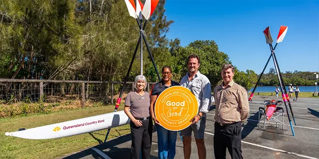 Community grant recipients standing beside a canoe holding a Queensland Country Good for Good Community Grants sign.