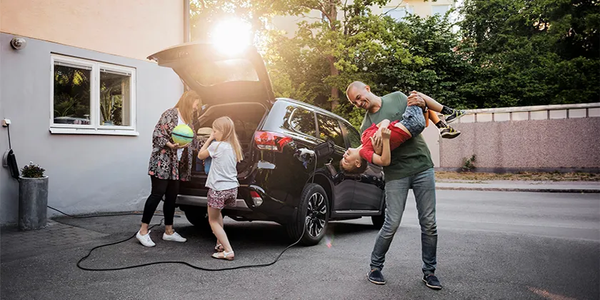 Adults and children unloading items from the boot of a car parked in a residential driveway.
