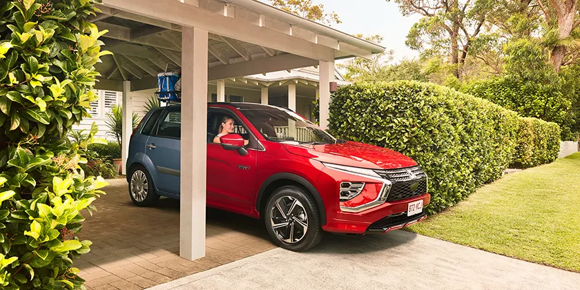An older blue car transitioning into a newer red car parked in a residential driveway, illustrating an upgrade to a new vehicle.