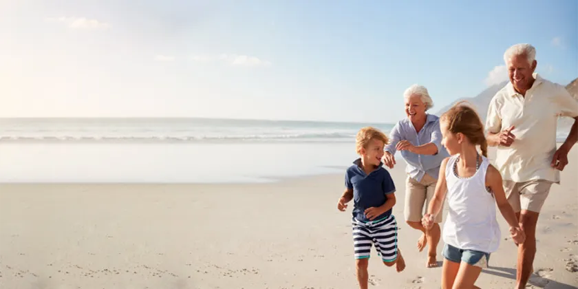 Group of adults and children walking together along a beach beside the ocean.